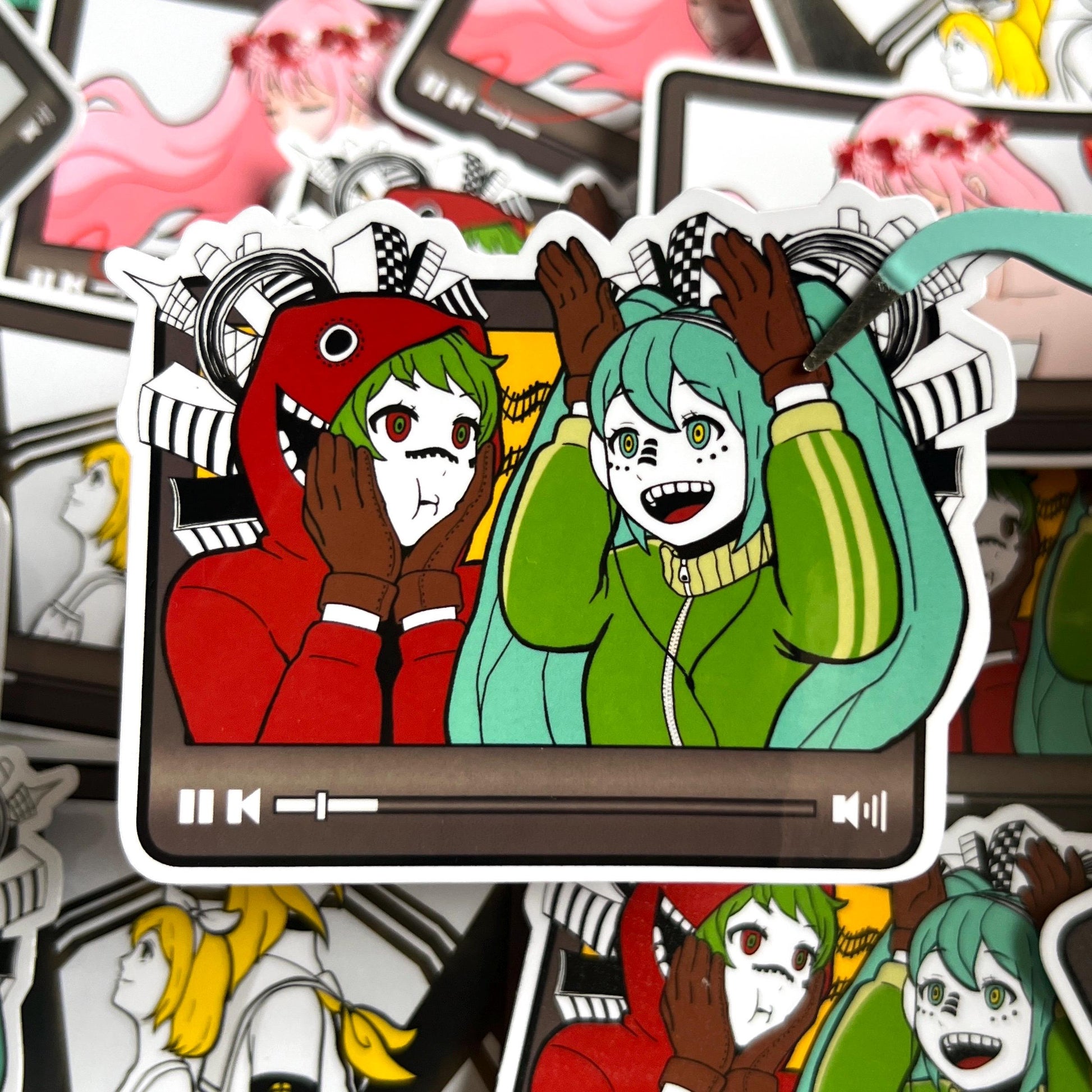 Sticker of Gumi and Hatsune Miku in Matryoshka shaped like a video player. Green hair anime girl dressed in a red hoodie with a yellow background. Teal hair anime girl in a green sweater with brown gloves.